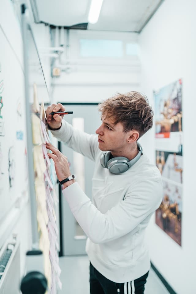 Um homem usando fones de ouvido está escrevendo em um quadro branco